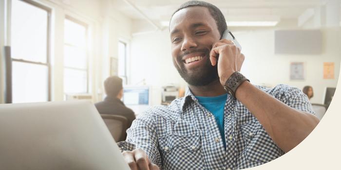 person sitting in an open office talking on their cell phone while looking at an open laptop