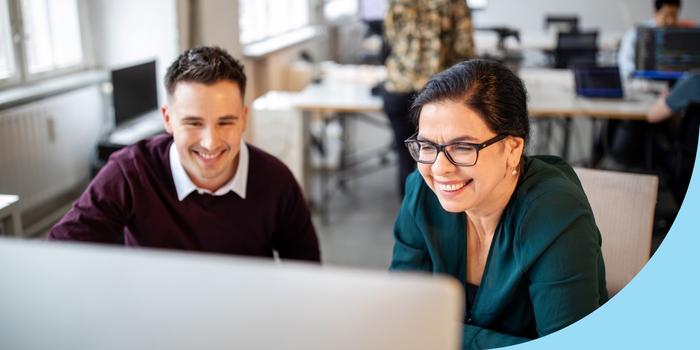 a younger and older coworker look at shared computer monitor