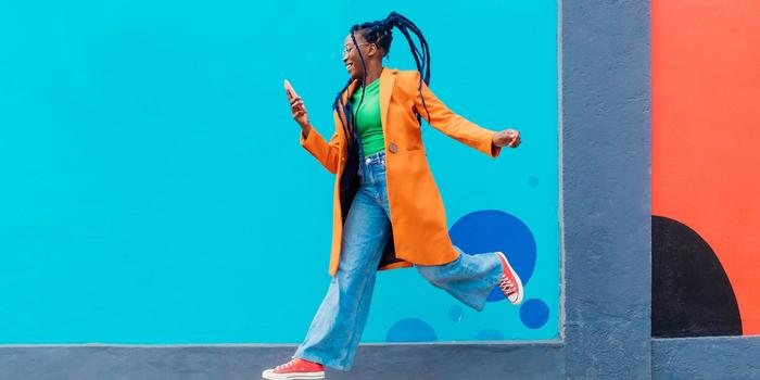 person in orange jacket taking a big step in front of a bright blue wall while looking at phone