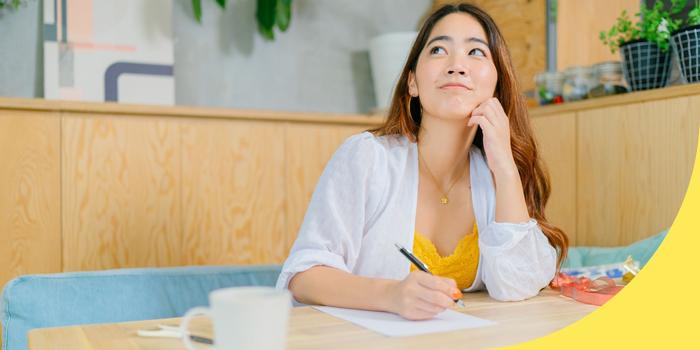 person sitting at a booth style table writing a thank you note