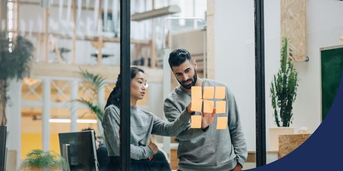 two people looking at sticky notes on a glass wall in an office