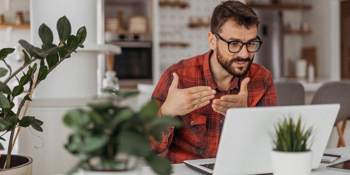 person in video interview sitting in front of an open white laptop on a white counter with three house plants in the foreground