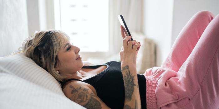person lying down on their bed holding a cell phone and looking at the screen