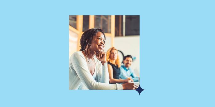 person sitting in a mentoring group smiling and looking hopeful with two other professionals visible behind her; the photo is placed against a light blue background with a navy blue star in one corner of the photo