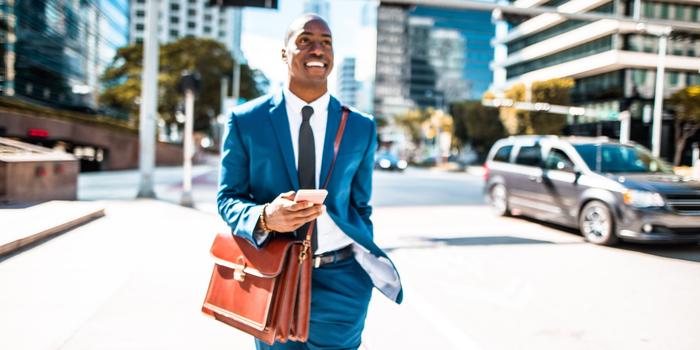 how to apply resume in linkedin person in blue business suit with brown leather bag walking through city, looking up from phone and smiling