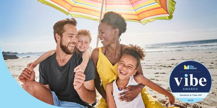 A family with small children smiling and embracing on the beach under an umbrella.