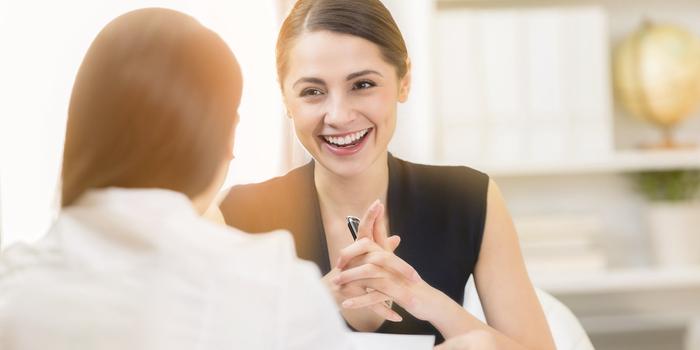 person smiling at a job interview facing the camera, while the interviewer has their back to camera