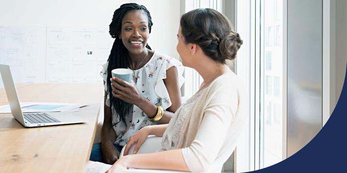 Two women sitting and talking in a conference room with an open laptop on the table