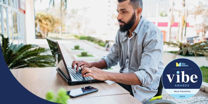 A man sitting at a table outdoors and working on a laptop.