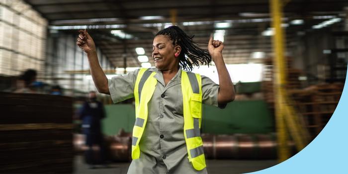 employee in a high-vis vest dancing in front of a blurred out factory floor