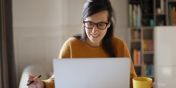 person sitting in front of their laptop at home while on a video call with a mug in one hand