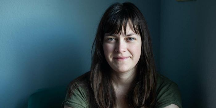 person with long brown hair in a dark green T-shirt