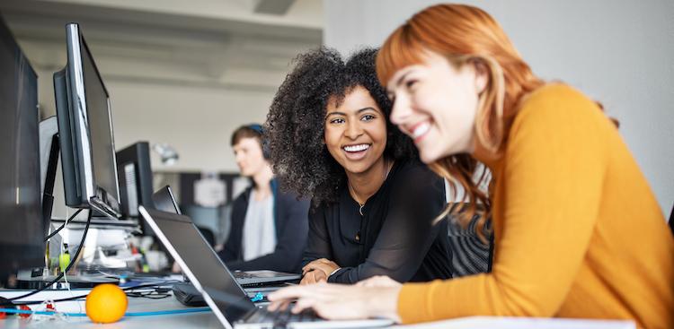 two women smiling and working at computers
