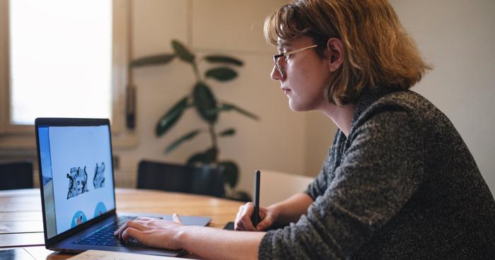 graphic designer drawing on a tablet while looking at laptop screen, with a plant in the background