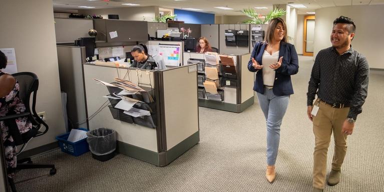 Two people walking past a row of cubicles in an office