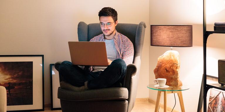 person working on laptop while sitting cross-legged on armchair