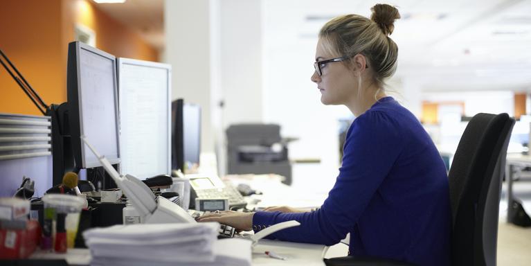 person sitting at desk with double computer monitors in office