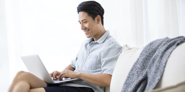 person on couch typing on laptop and smiling