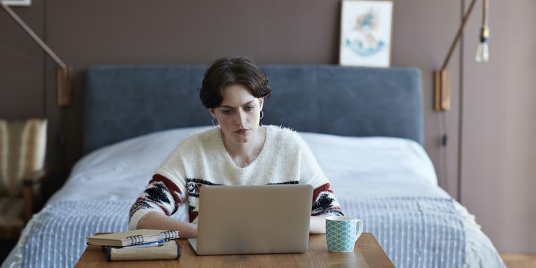 person on laptop in front of bed