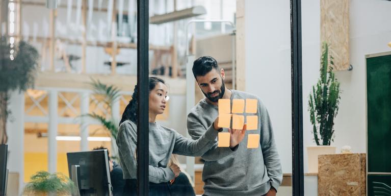 two people looking at sticky notes on a glass wall