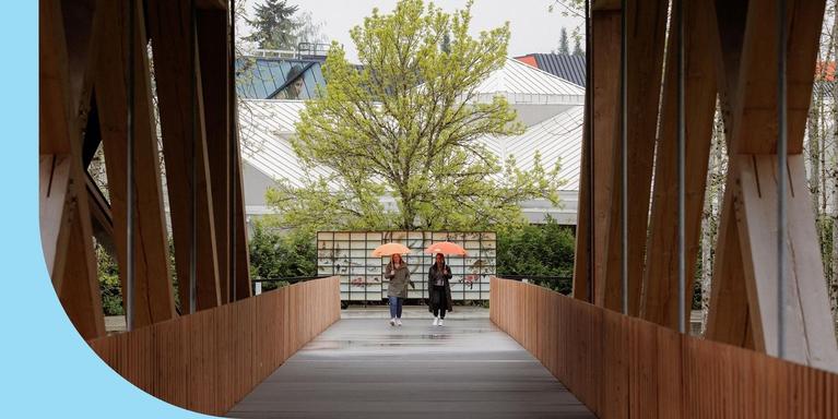 Two employees walking around Nike’s HQ campus, each holding up an orange umbrella