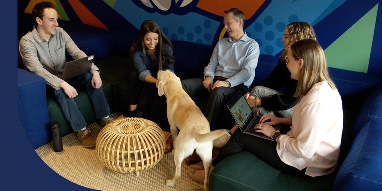 Upside employees sitting on a couch and petting a dog in the office.