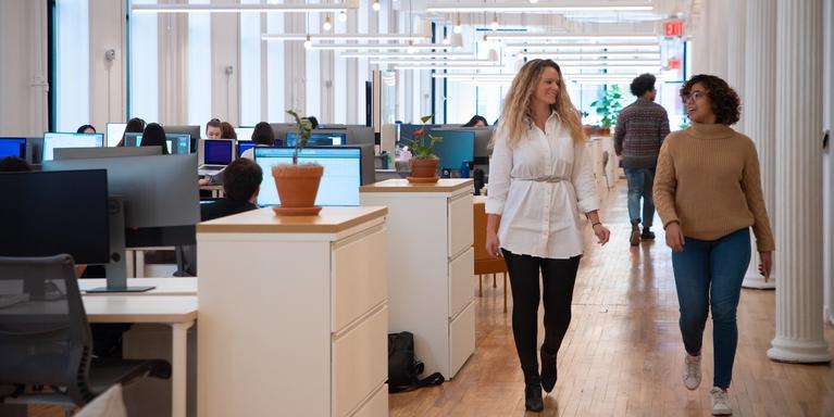 two people walking together in a open plan office space