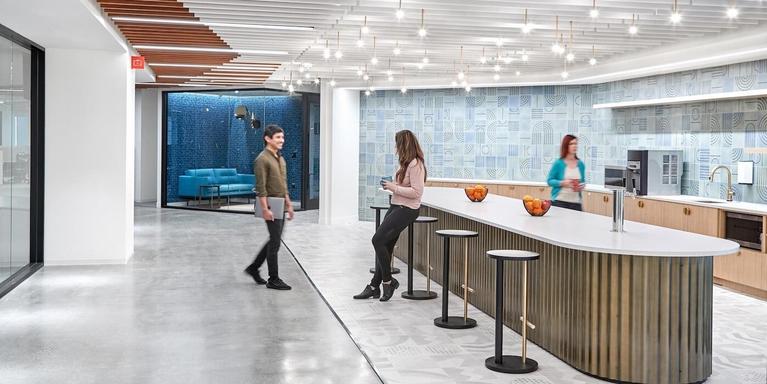 Employees in an office kitchen area with an island and barstools.