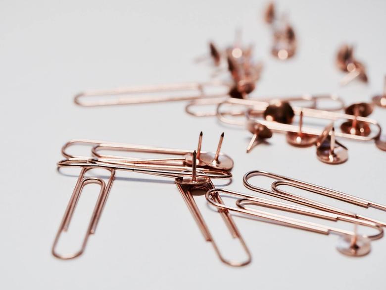 rose gold paper clips and thumbtacks scattered on a surface