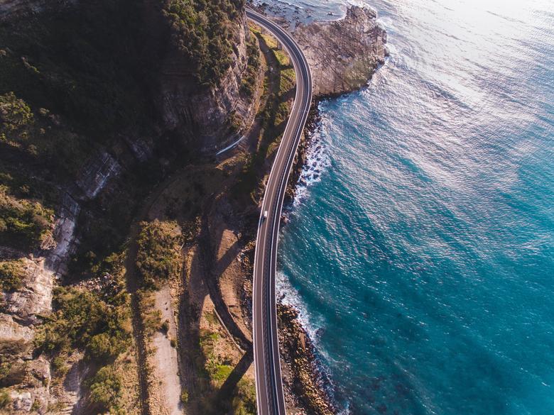 aerial view of a car on a road with a cliff on one side and water on the other