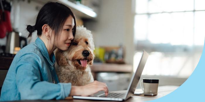 person sitting at a kitchen table with a dog next to them, both looking at a laptop