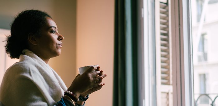 person sitting at home holding a mug and staring out the window