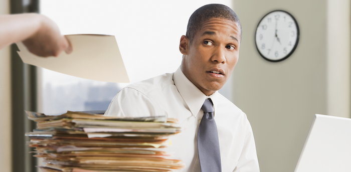 person sitting with his laptop and a big pile of files being handed another folder