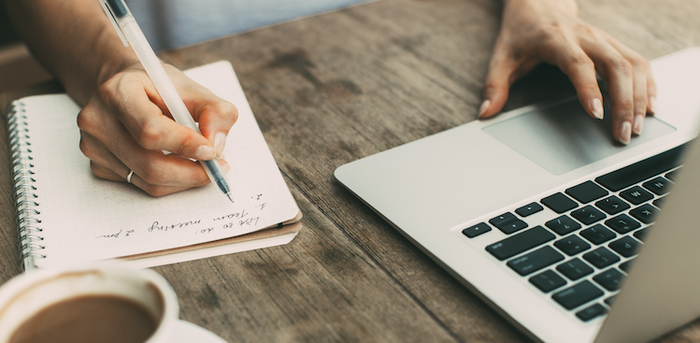 person working on laptop and writing in notebook