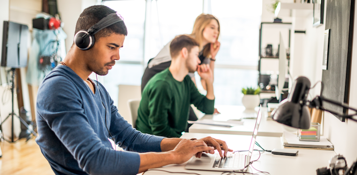 person wearing headphones while working on a laptop in an open office