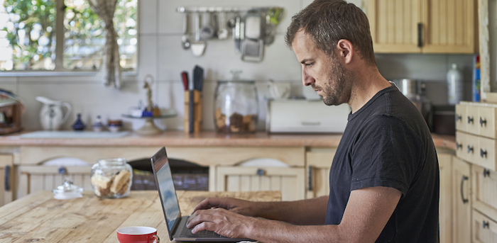 person sitting at a kitchen table working on a laptop