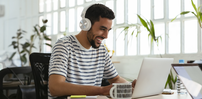 person working on a laptop with headphones, a mug, and various supplies on their desk