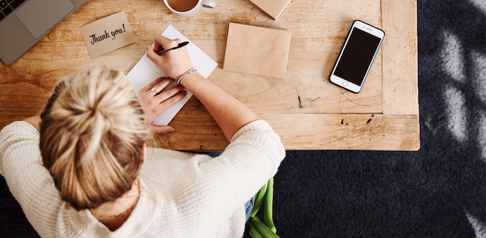 person sitting at a table writing a thank you card