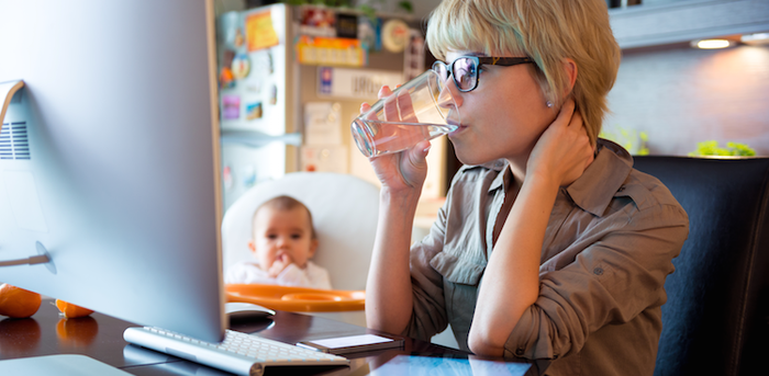 person working at home with baby sitting in chair nearby