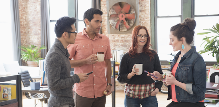 co-workers holding coffee cups and phones standing and chatting in an office