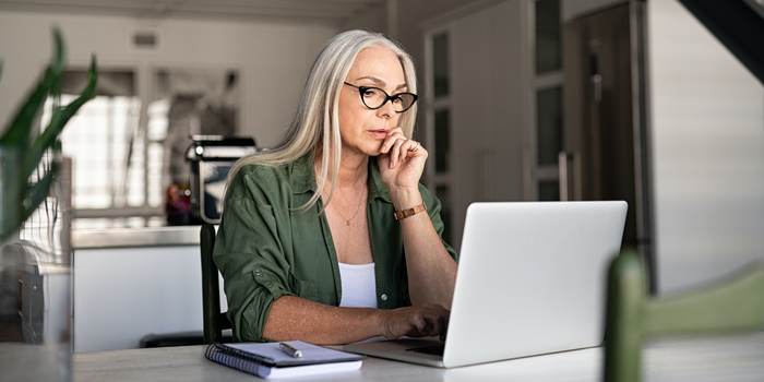 person sitting at home working on a laptop with a notebook and pen nearby