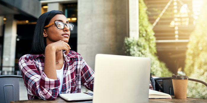 college student sitting at a table outside on campus with a notebook, book, laptop, and coffee cup