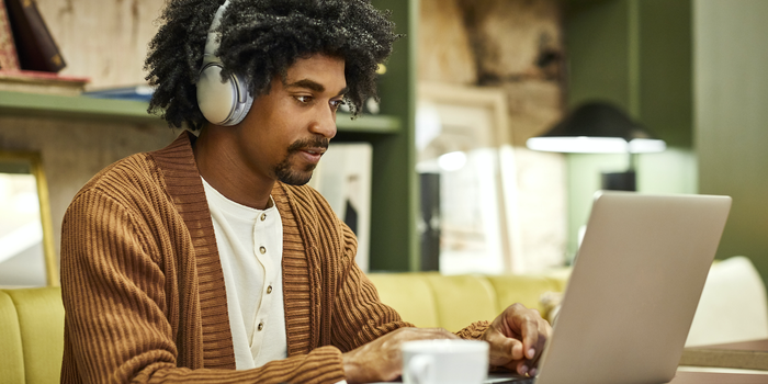 Person sitting at a desk, wearing headphones and typing on laptop