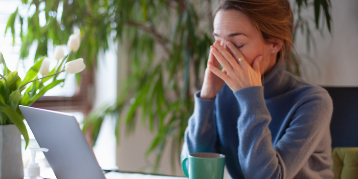 person working from home sitting in front of laptop rubbing their eyes