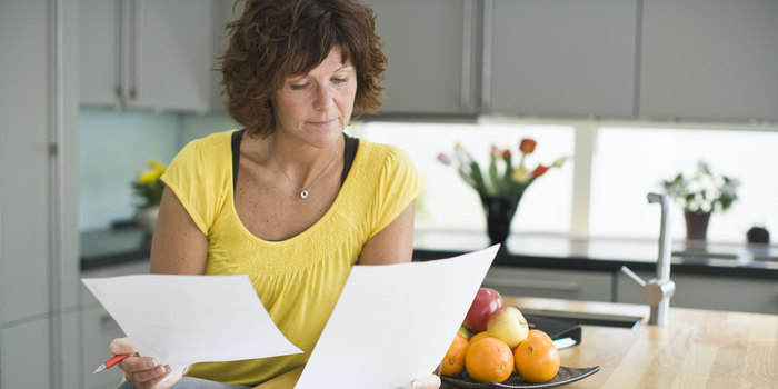 person sitting in their kitchen holding and looking at two sheets of paper