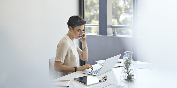 person sitting at a desk working on a laptop and speaking on a cell phone