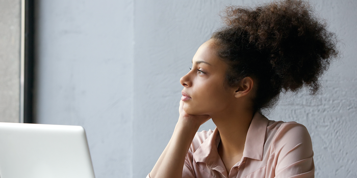 person sitting in front of a laptop staring out the window and thinking