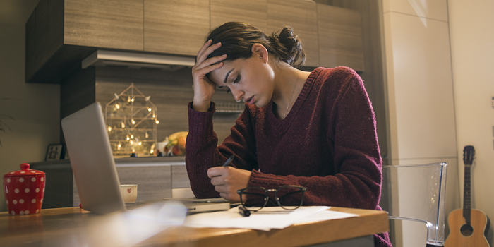 exhausted person sitting at home working in front of a laptop with their head in their hand