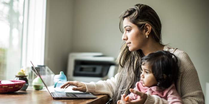 parent sitting at home working on a laptop while holding a baby on their lap