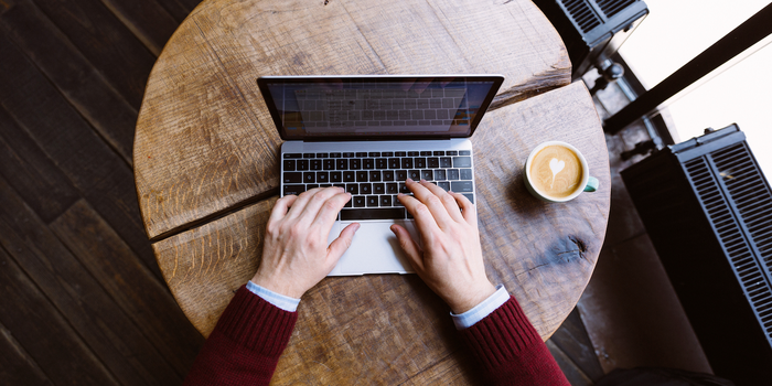 hands typing on an open laptop with a latte in a cup nearby